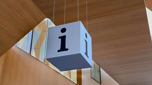 Ein blauer Würfel mit einem i für Information hängt von einer Holzdecke