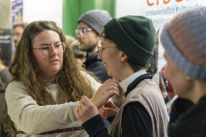 Das Publikum hat am Eröffnungstag die Möglichkeit, einen weißen Herrenkragen anzuprobieren. Foto: Roland Pokorny [22.01.2025]. (öffnet Vergrößerung des Bildes)