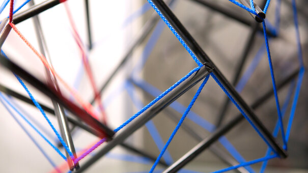 Datailansicht einer Struktur aus Fäden und Stäben, die so angeordnet sind, dass sie sich gegenseitig stabilisieren, ohne sich direkt zu berühren.
