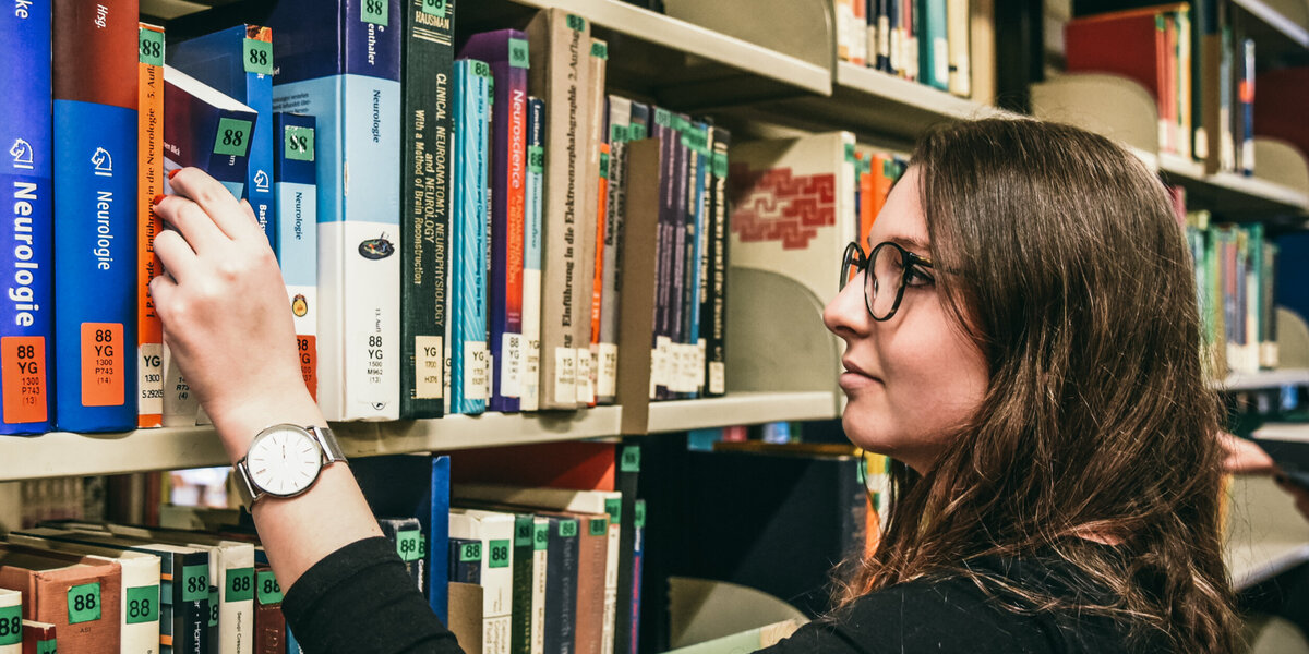 Eine junge Frau wählt an einem Bücherregal im Lesesaal Biologie der Universität Regensburg ein Buch aus.