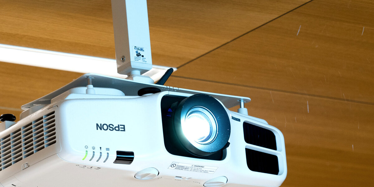 Ein an der holzvertäfelten Hörsaal-Decke installierter Beamer.