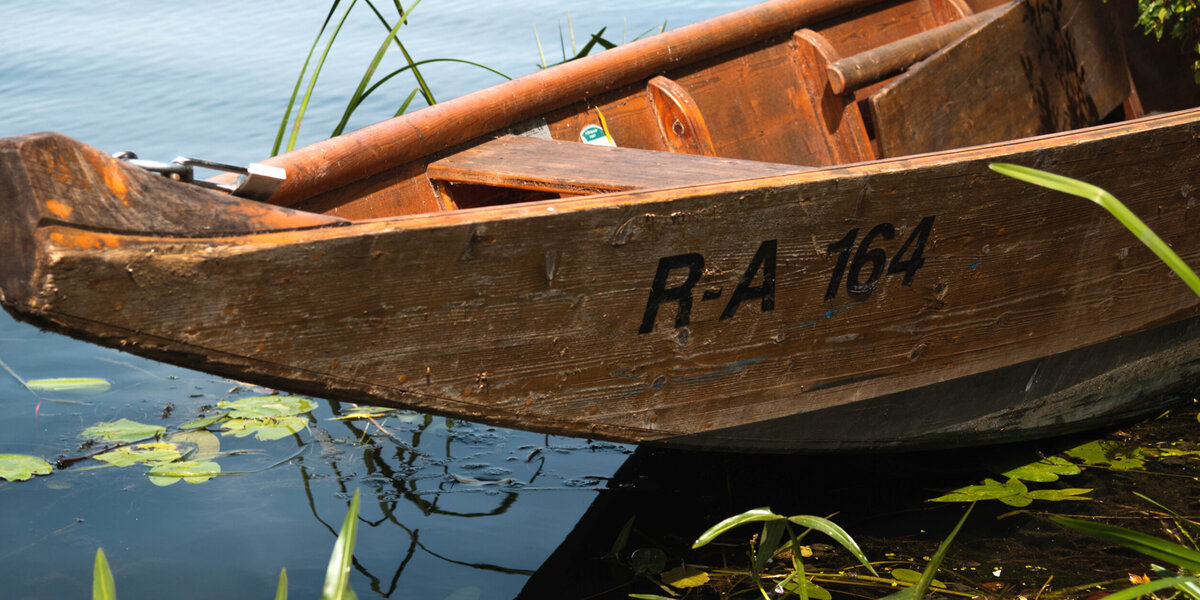 Ein Holzboot in einer dunklen, ruhigen Wasserfläche, auf der Seerosen treiben.