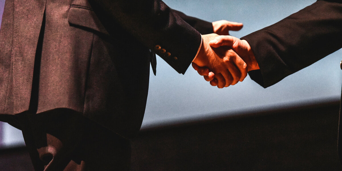 Zwei Personen in dunklen Anzügen schütteln sich die Hände.