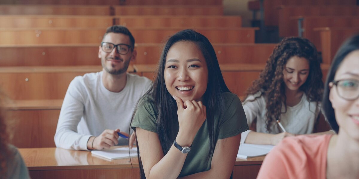 Zu sehen ist ein Klassenraum mit weiblichen und männlichen Studierenden, die lächeln. 
