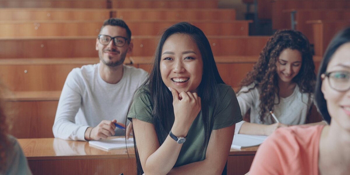 Zu sehen ist ein Klassenraum mit weiblichen und männlichen Studierenden, die lächeln. 