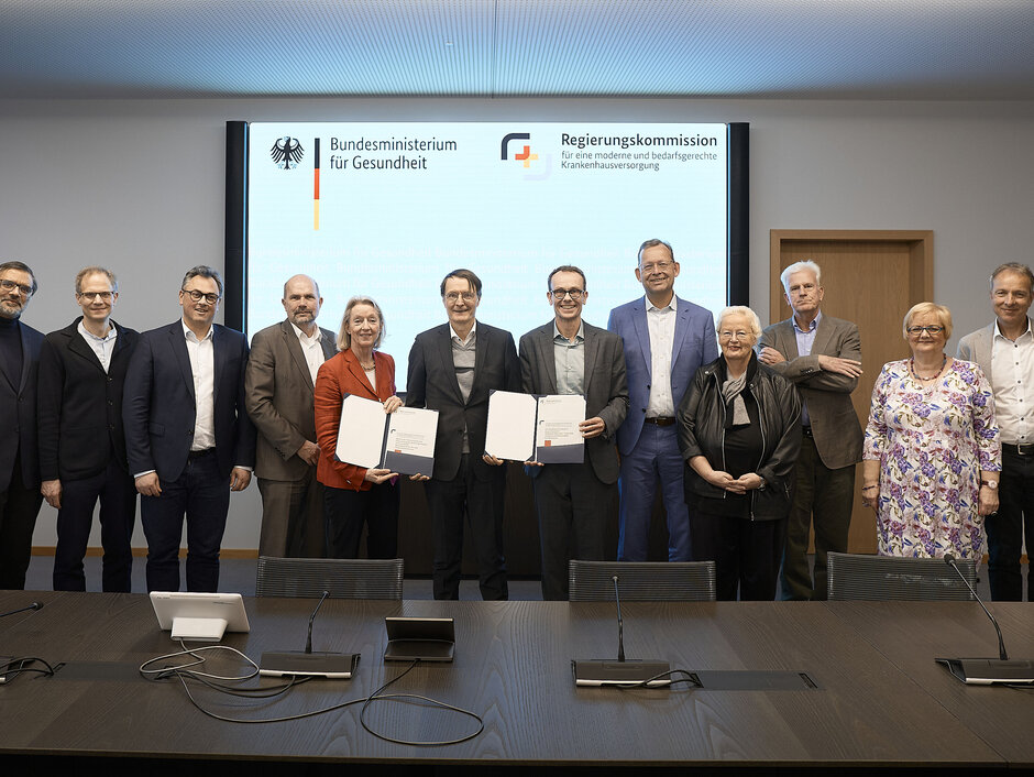 Gruppenfoto der Kommissionsmitglieder mit Karl Lauterbach in einem Konferenzraum vor einer Leinwand. (öffnet Vergrößerung des Bildes)