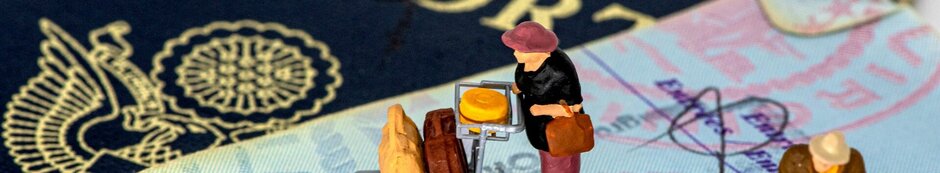 2 Miniaturfiguren mit Gepäckwagen sind auf einem Reisepass aufgestellt