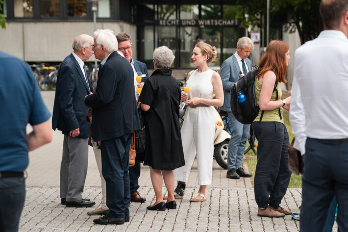 Mehrere Personen in teils festlicher Garderobe, die Sektflöten in der Hand halten, sind miteinander ins Gespräch vertieft. (öffnet Vergrößerung des Bildes)