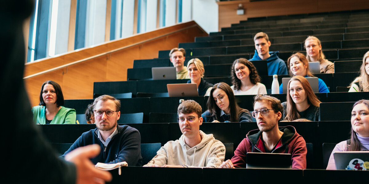 Studierende in einem Hörsaal der Universität Regensburg hören dem Vortrag eines Dozenten zu.