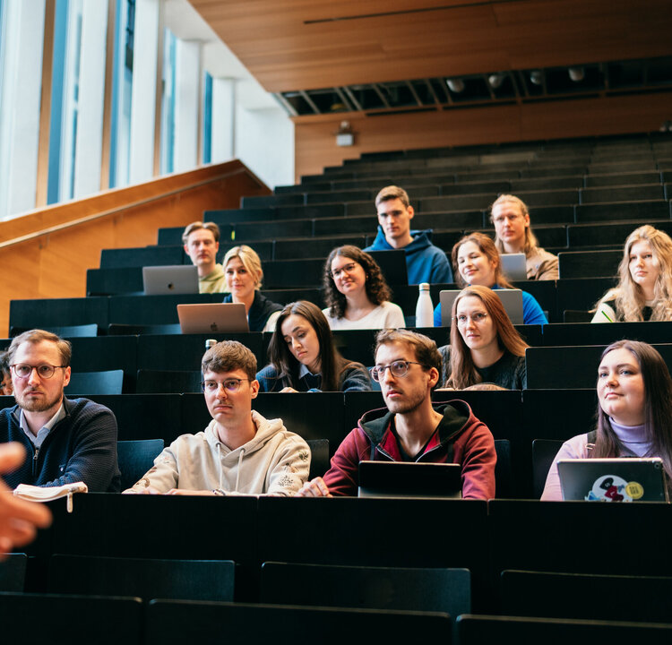 Studierende in einem Hörsaal der Universität Regensburg hören dem Vortrag eines Dozenten zu.
