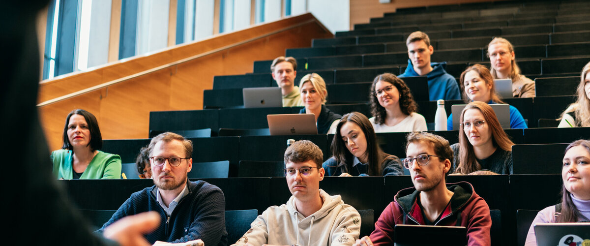 Studierende in einem Hörsaal der Universität Regensburg hören dem Vortrag eines Dozenten zu.