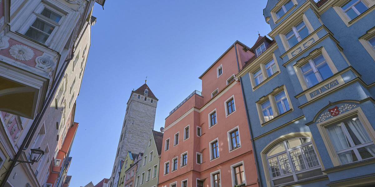 Bunte historische Häuserfassaden in der Regensburger Altstadt vor blauem Himmel aus der Froschperspektive fotografiert.