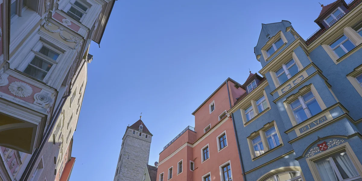 Bunte historische Häuserfassaden in der Regensburger Altstadt vor blauem Himmel aus der Froschperspektive fotografiert.