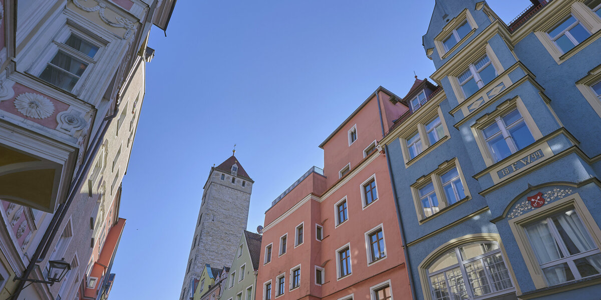 Bunte historische Häuserfassaden in der Regensburger Altstadt vor blauem Himmel aus der Froschperspektive fotografiert.