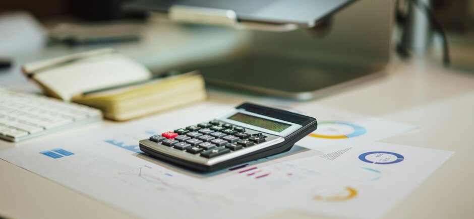 Schreibtisch mit Taschenrechner Tabellen, Laptop und Notizbuch