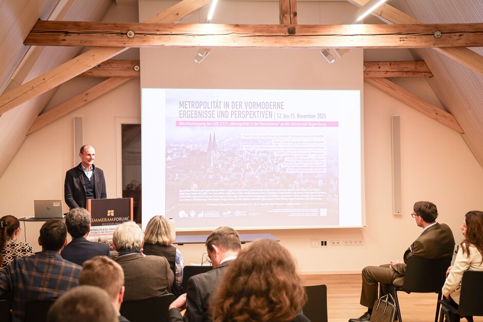 Publikum in Hörsaal von hinten, blickt auf älteren Herrn am Rednerpult.