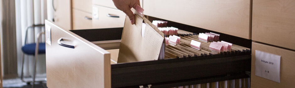 Person, die etwas aus einem Aktenschrank an der Uni Regensburg herausnimmt