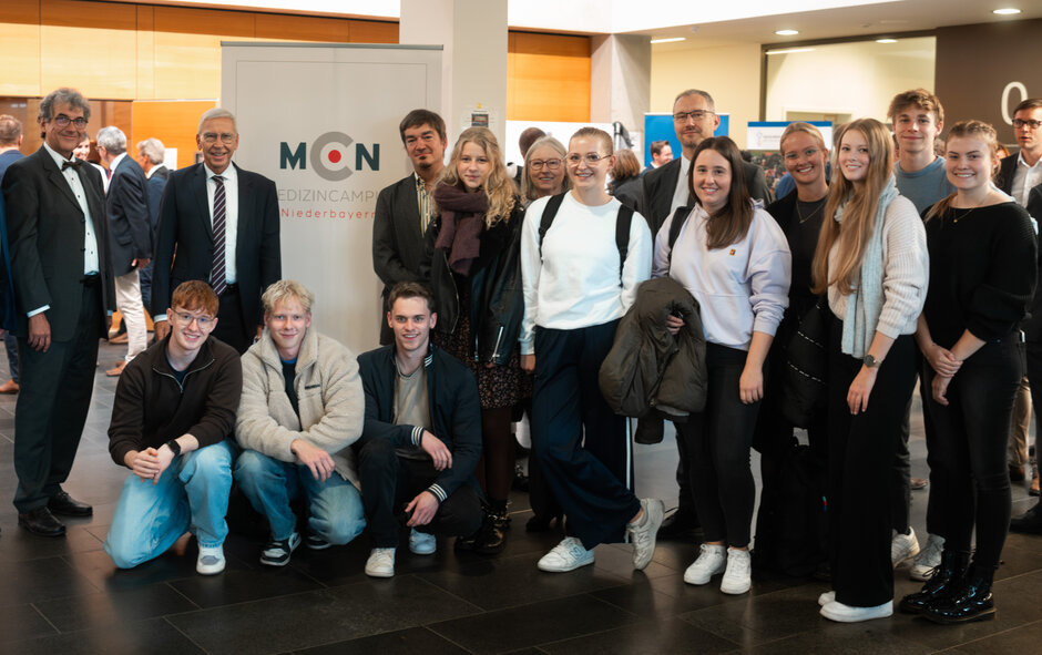 Studierende posieren gemeinsam mit Präsident Hebel und Vizepräsident Tamm vor einem Banner des MedizinCampus Niederbayern