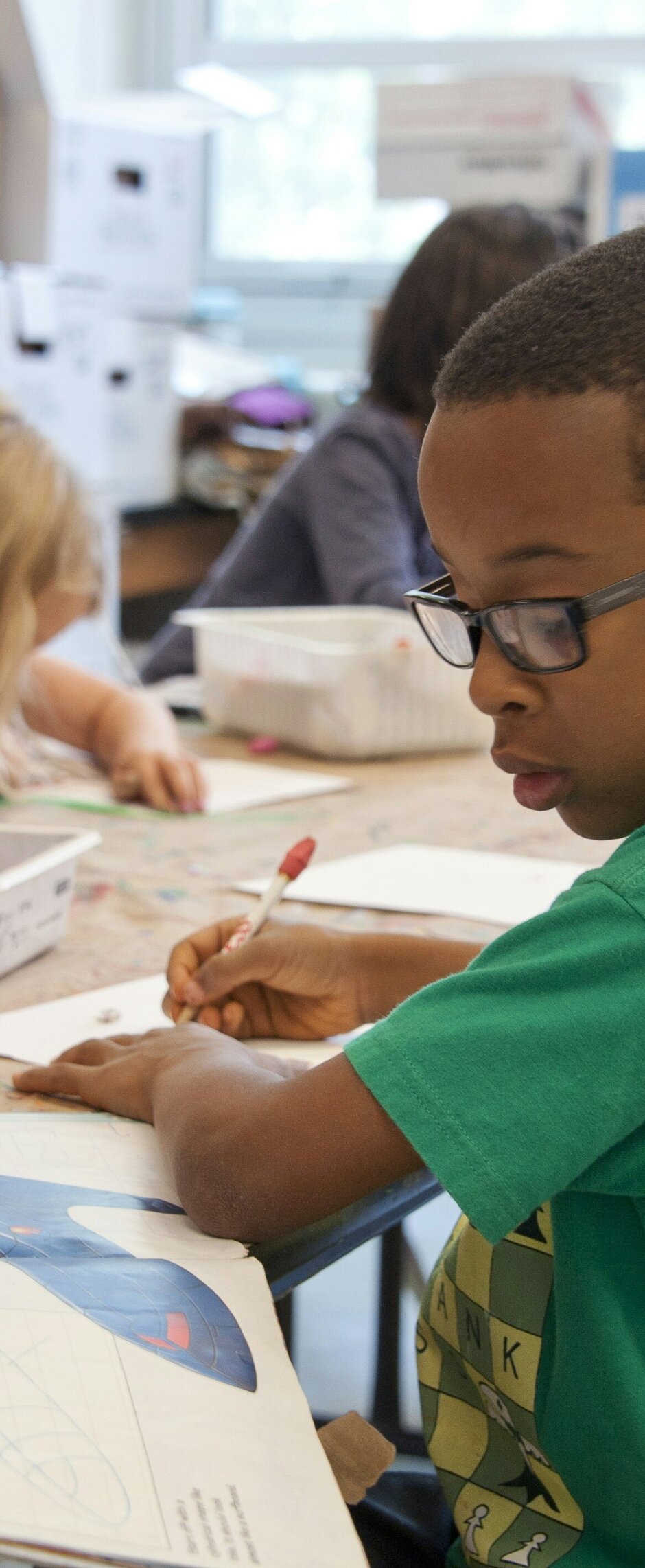 Mehrere Schulkinder sitzen an einem langen Tisch und arbeiten mit Stiften in Heften