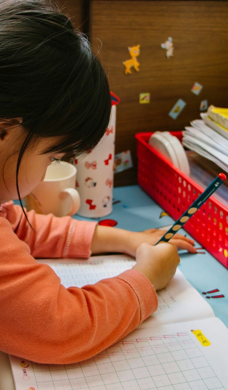 Mädchen im Kindergartenalter sitzt an einem Tisch und schreibt