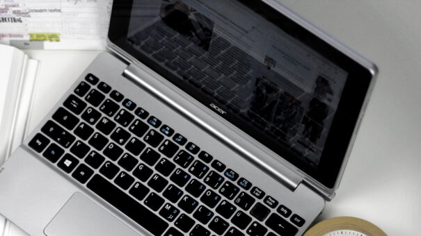 Eine Studentin sitzt an einem Schreibtisch, auf dem ein Laptop, ein Wecker, auf aufgeschlagenes Buch und ein Vorlesungsskript liegen.