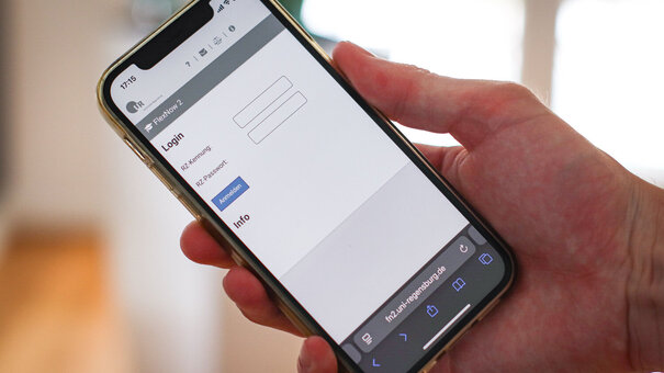 Eine Hand hält ein Smartphone. Auf dem Bildschirm ist eine Anmelde-Maske zu sehen.