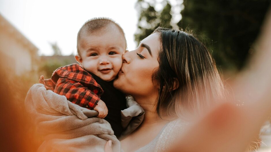 Frau hebt Kleinkind hoch und gibt ihm einen Kuss