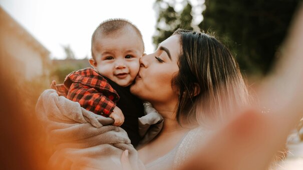 Frau hebt Kleinkind hoch und gibt ihm einen Kuss