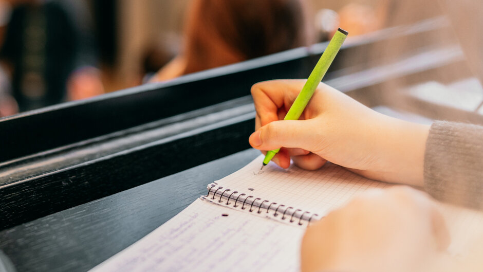 Eine Hand schreibt mit einem grünen Faserschreiber in ein Ringbuch