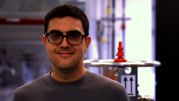 Porträt eines Mannes mit Brille, im Hintergrund physikalische Versuchsanordnung