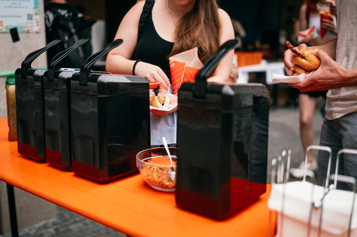 Eine Person steht vor dem Ketchupspender und füllt Soße auf ihren Hotdog. (öffnet Vergrößerung des Bildes)