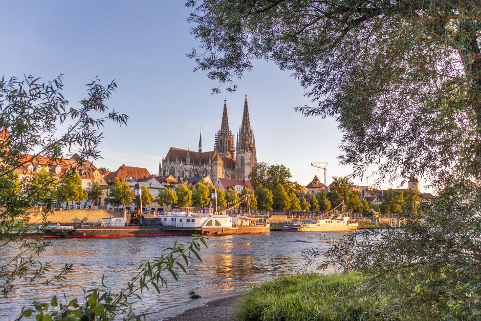 Blick auf die Donau, das südliche Ufer, Ausflugsschiffe und die Regensburger Altstadt. Im Hintergrund die Domspitzen.