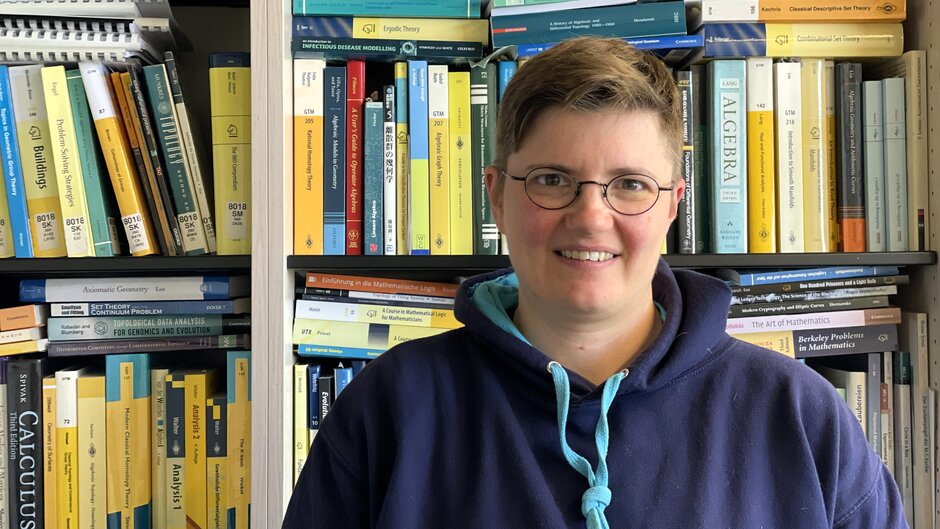 Woman with glasses and short hair in blue hoody in front of bookshelves. (external link, opens in a new window)