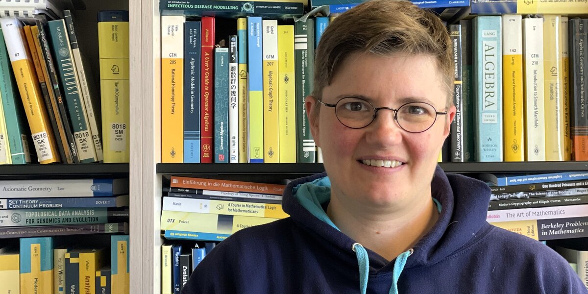Woman with glasses and short hair in blue hoody in front of bookshelves.