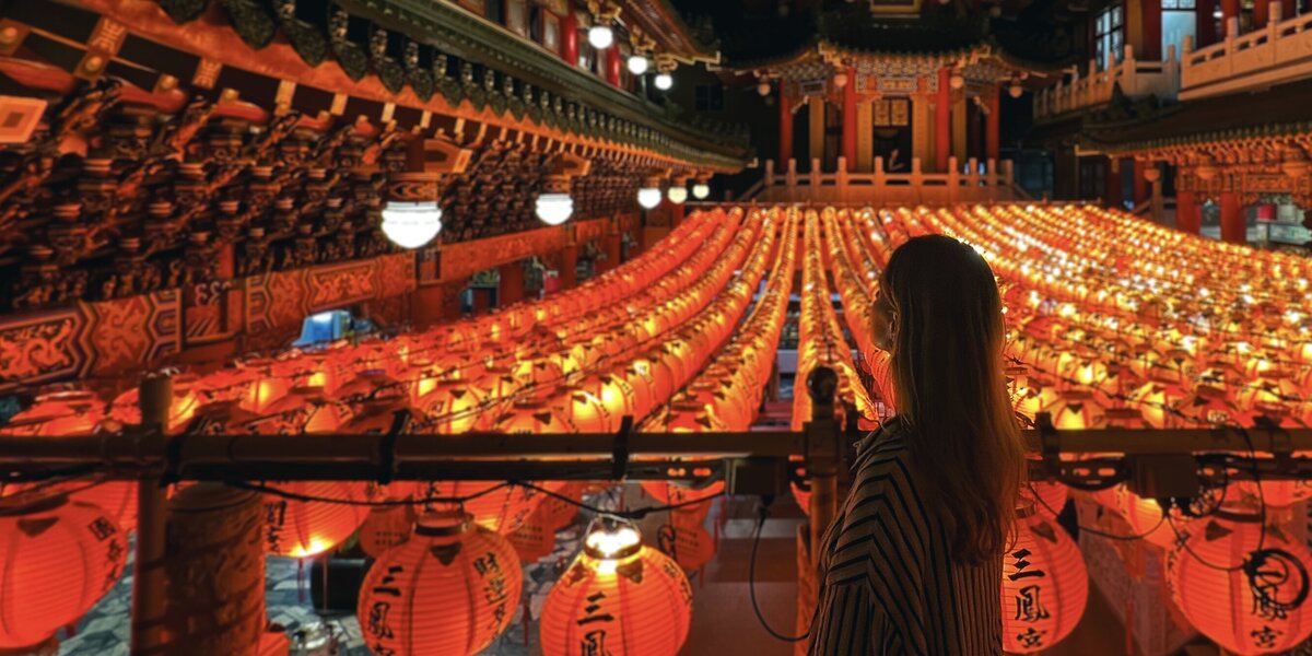 Eine Frau steht bei Nacht vor einem asiatischen Tempel. Zahlreiche orangefarbnene Lampions schmücken den Vorplatz.