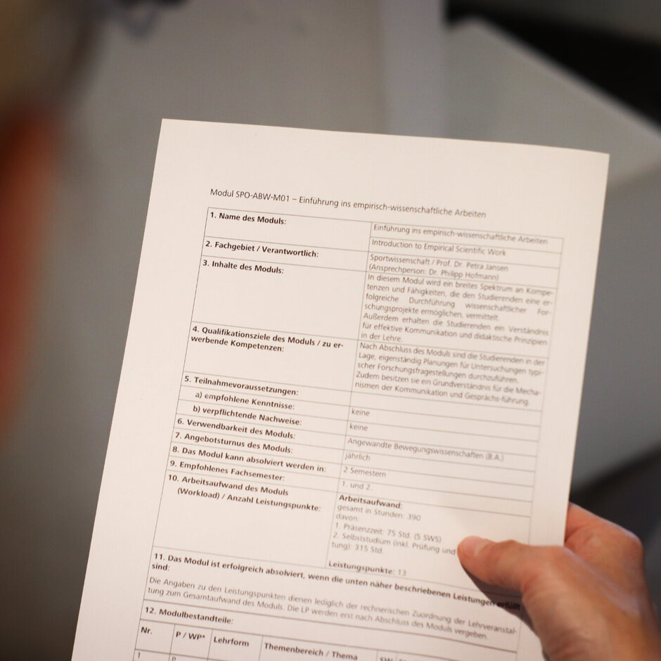 Eine Hand hält ein bedrucktes Blatt in der Hand. Das Blatt ist überschrieben mit „Modul SPO-ABW-M01 – Einführung ins empirisch-wissenschaftliche Arbeiten“