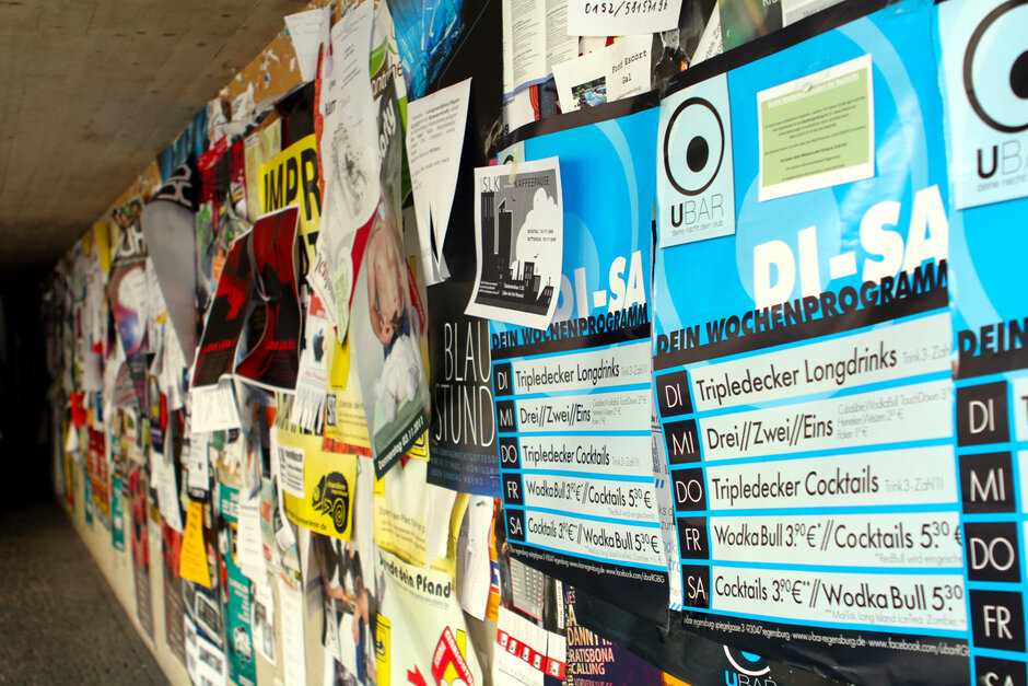 Plakatierfläche an der Universität Regensburg mit einem bunten Mix an Plakaten, Flyern und Abreisszetteln