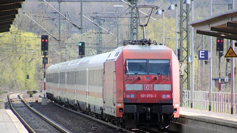 Man sieht einen roten Regionalzug in einen Bahnhof einfahren. 