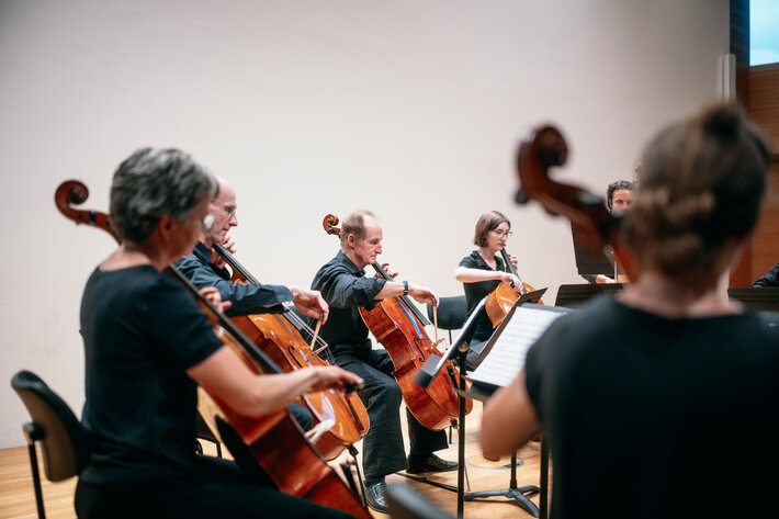 Sechs Personen sitzen im Halbkreis auf der Bühne und spielen Cello. (öffnet Vergrößerung des Bildes)