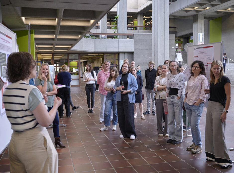 Zahlreiche Menschen in Foyer, gruppieren sich um Stellwände, eine Person spricht.