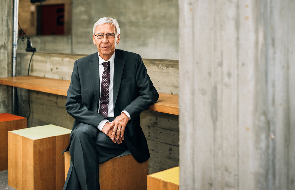 UR-Präsident Prof. Dr. Hebel sitzt auf einem der farbenfroh bezogenen Holz-Hocker auf der Galerie des Auditorium maximum