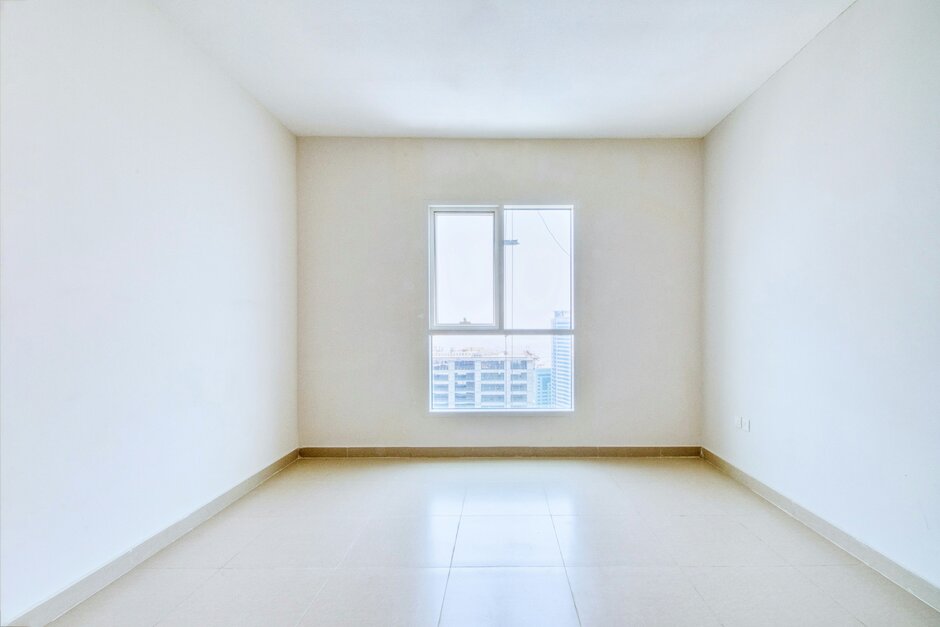 Zu sehen ist ein unmöbliertes Zimmer mit weißen Wänden und einem Fenster in der Mitte. 