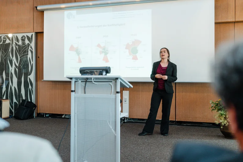 Ein Frau steht vor einer Powerpoint-Folie und hält einen Vortrag.  (öffnet Vergrößerung des Bildes)
