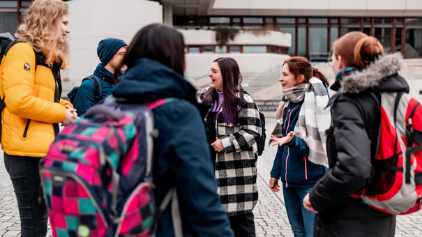 Eine Gruppe von Studieren steht zusammen am Campus der Universität Regensburg und unterhält sich.