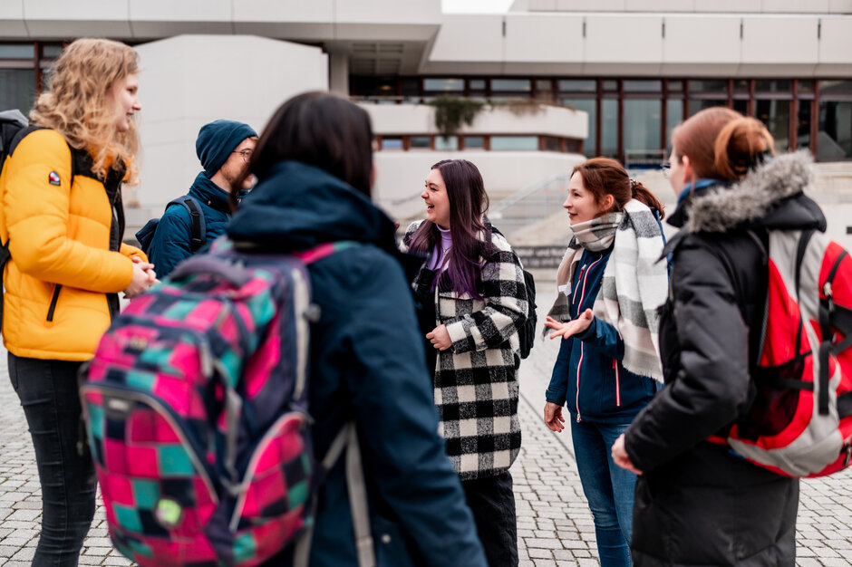 Eine Gruppe von Studieren steht zusammen am Campus der Universität Regensburg und unterhält sich.