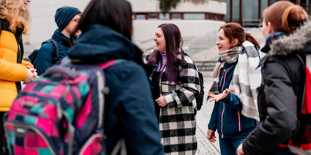 Eine Gruppe von Studieren steht zusammen am Campus der Universität Regensburg und unterhält sich.