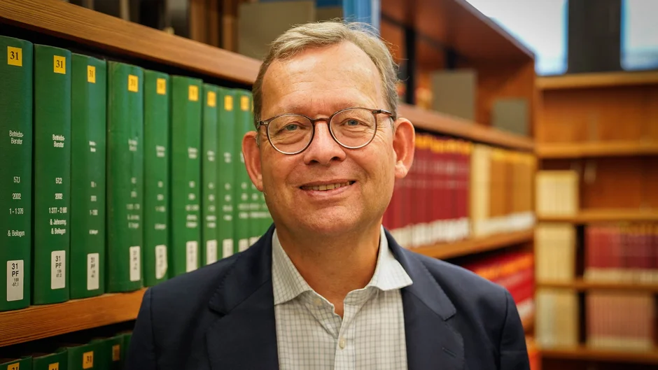 Lächelnder Mann mit Brille stehend vor Bücherregal
