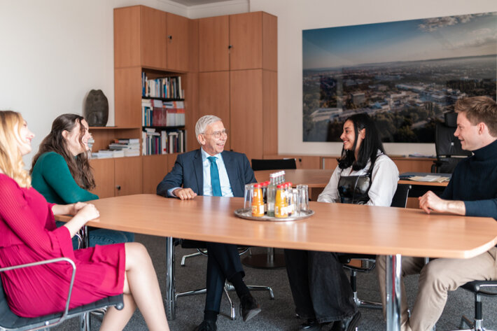Fünf Personen sitzen um einen Besprechungstisch und unterhalten sich entspannt. (öffnet Vergrößerung des Bildes)