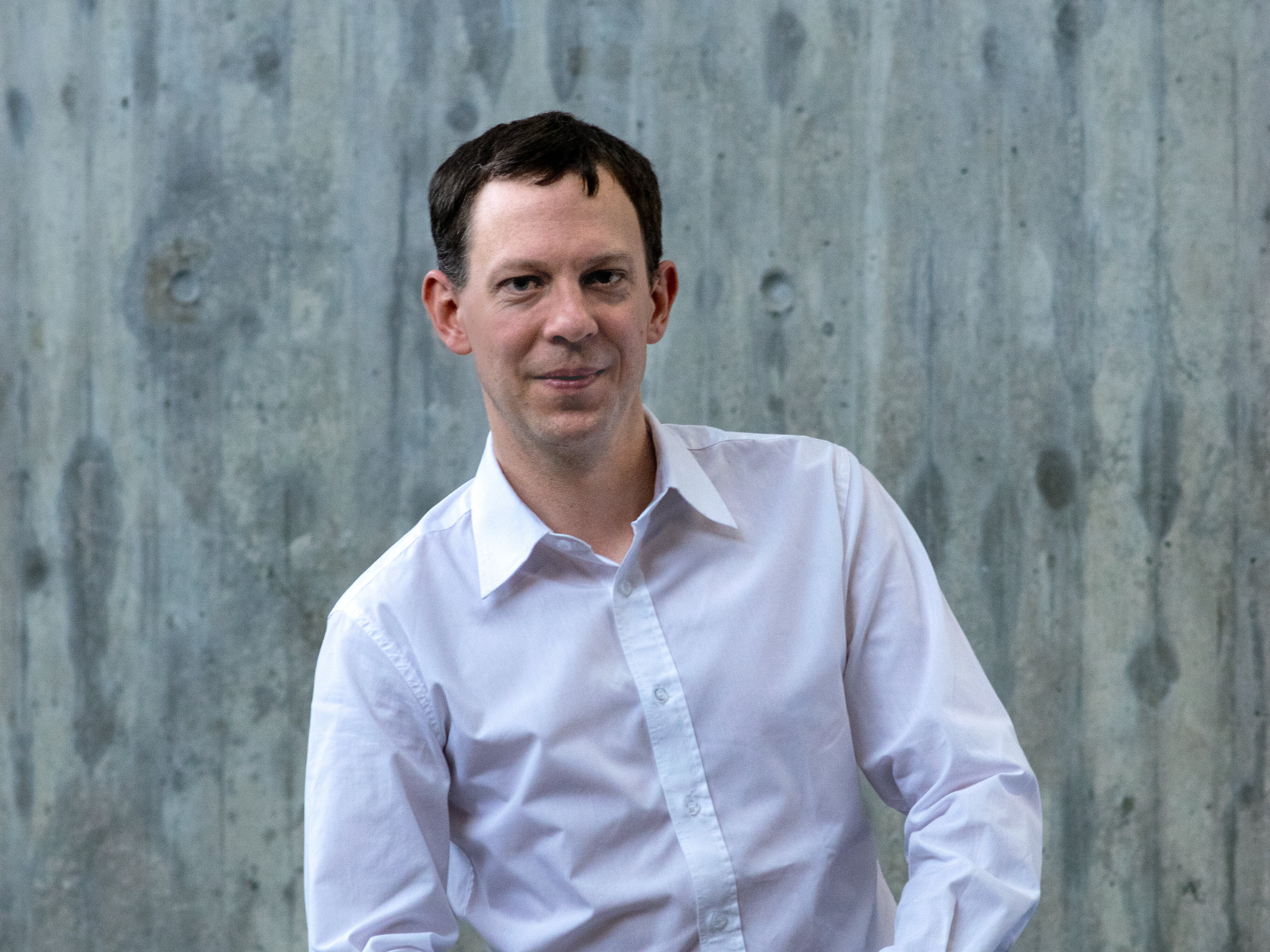 Ein Mann mit hellblauem Hemd lächelt in die Kamera. (opens enlarged image)