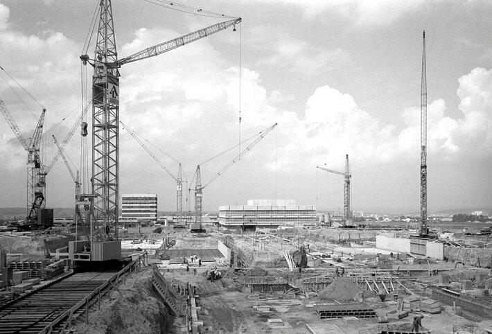 Schwarz-Weiß-Foto einer Baustelle mit vielen Baugruben, Bodenplatten und sieben Baukränen. (opens enlarged image)